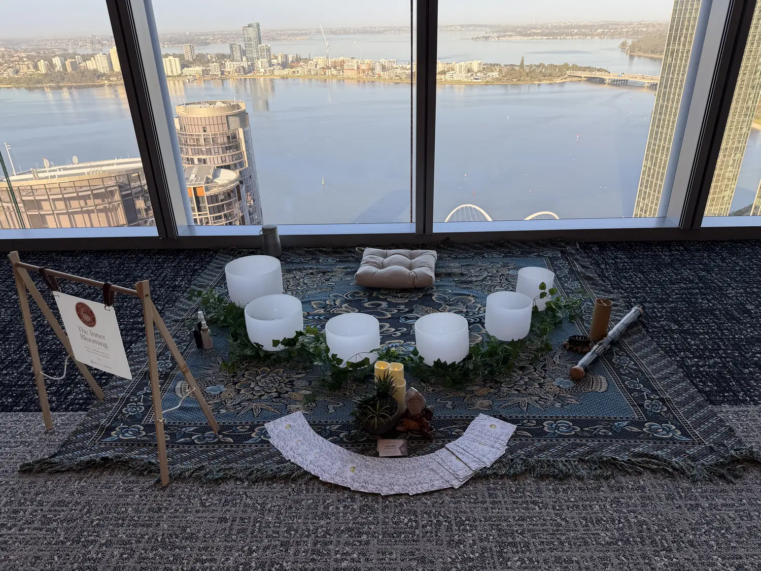 Crystal singing bowls set up for a workplace sound bath beside a high-rise window overlooking the Swan River, Perth